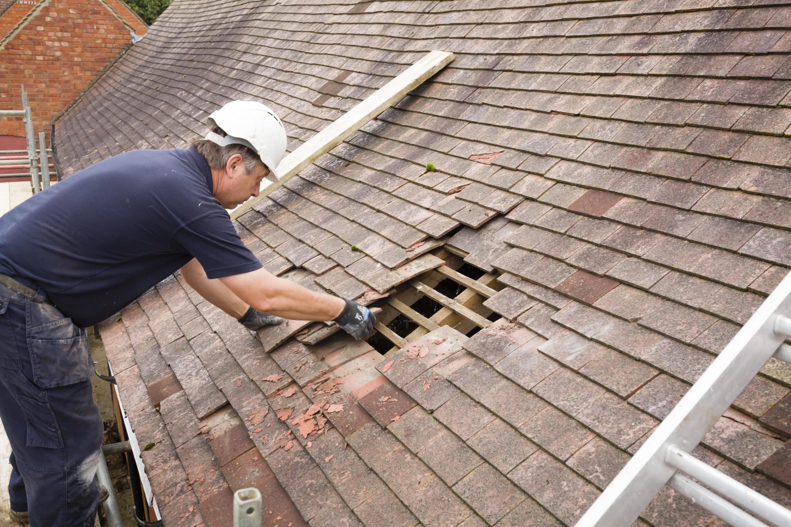 Builder removing old clay tiles from a pitched roof UK